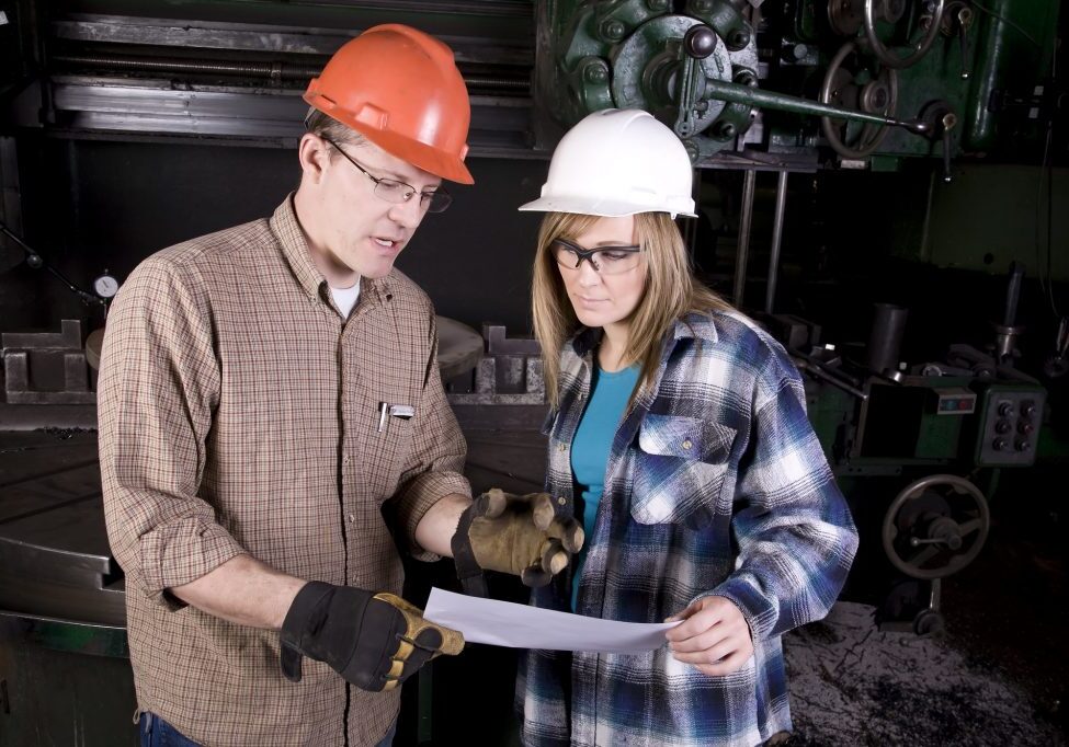 A man and woman working together on a project on a machine.  The man is explaining what is expected.