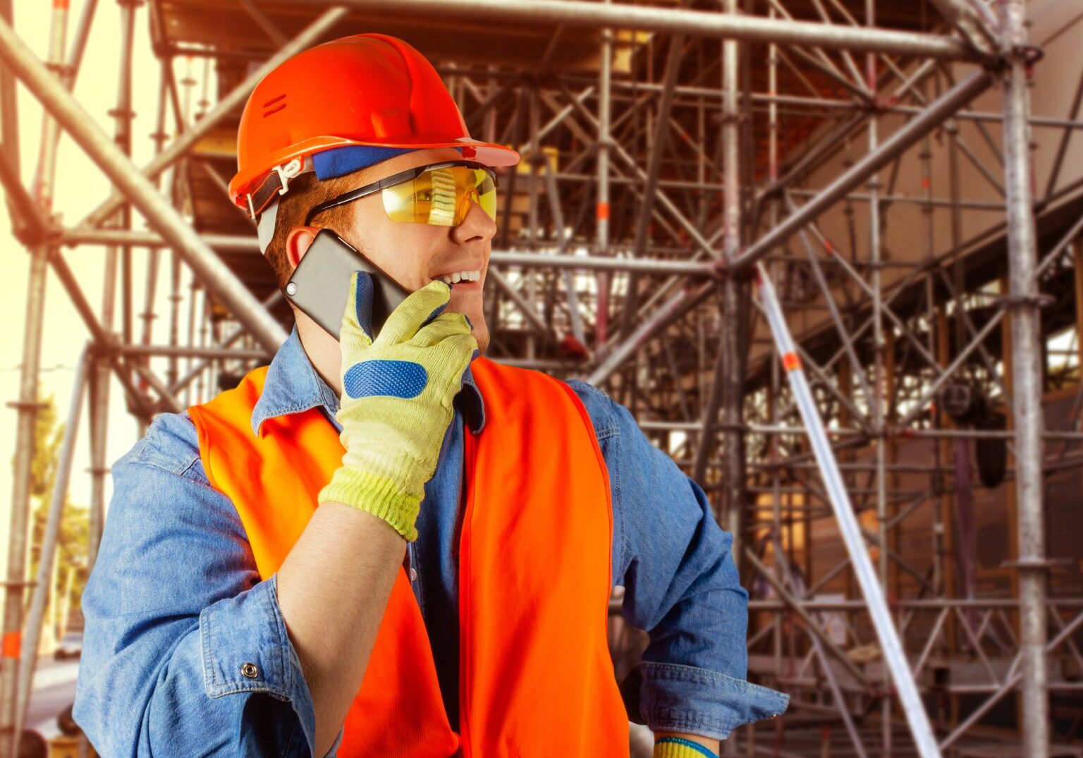 Photo of a male worker in protection outfit speaking on a phone on a constrauction area background.